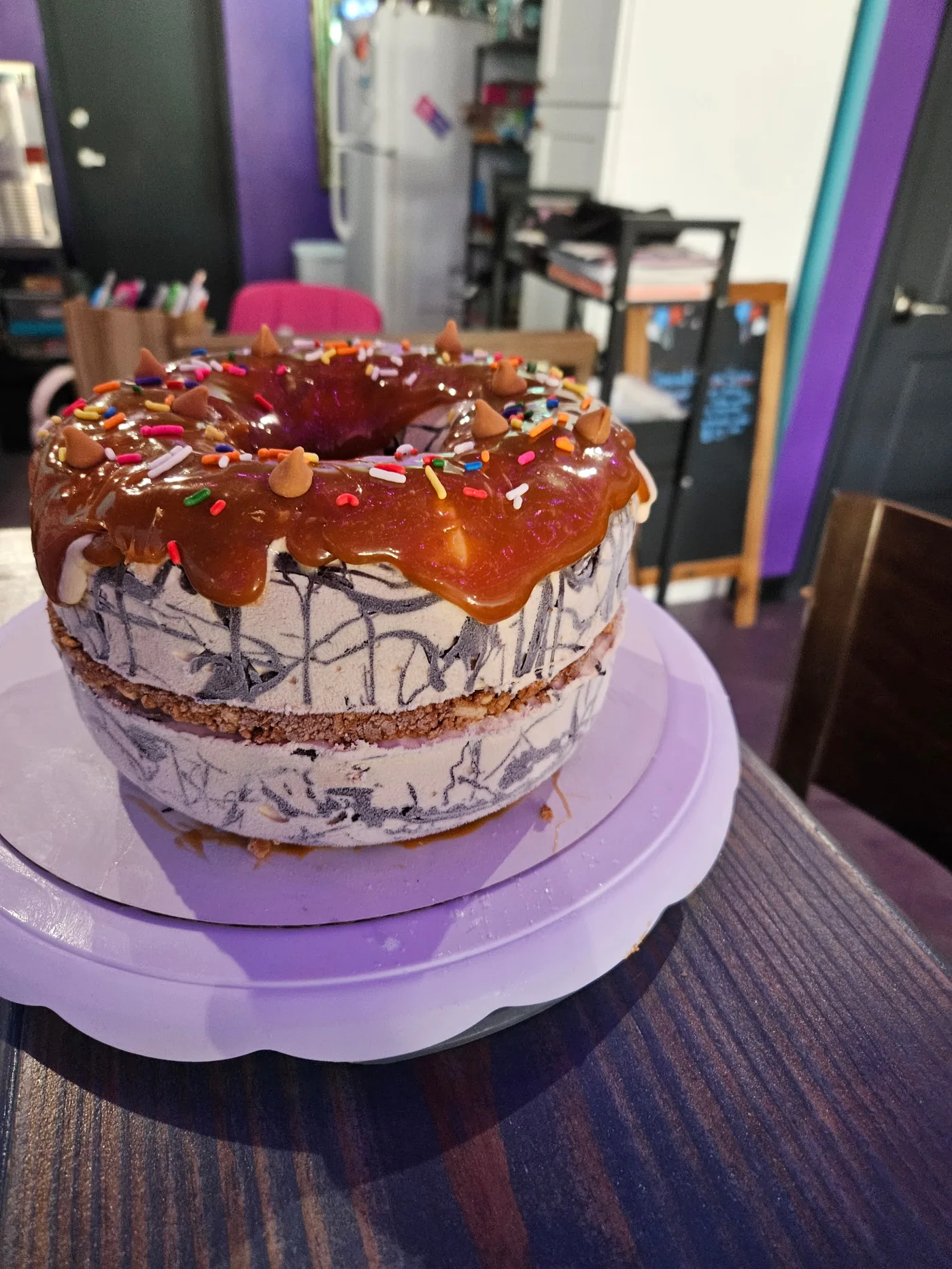 House-made ice cream bundt cake topped with caramel drizzle, sprinkles, and peanut butter cups, on a purple turntable