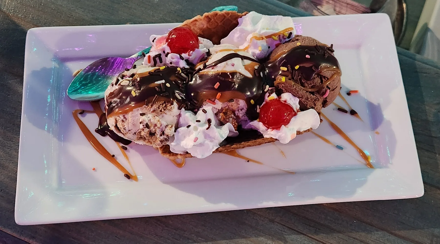 Ice Cream Taco — three scoops in a waffle-cone taco shell, drizzled with hot fudge, caramel, sprinkles, whipped cream, and two cherries on a rectangular plate