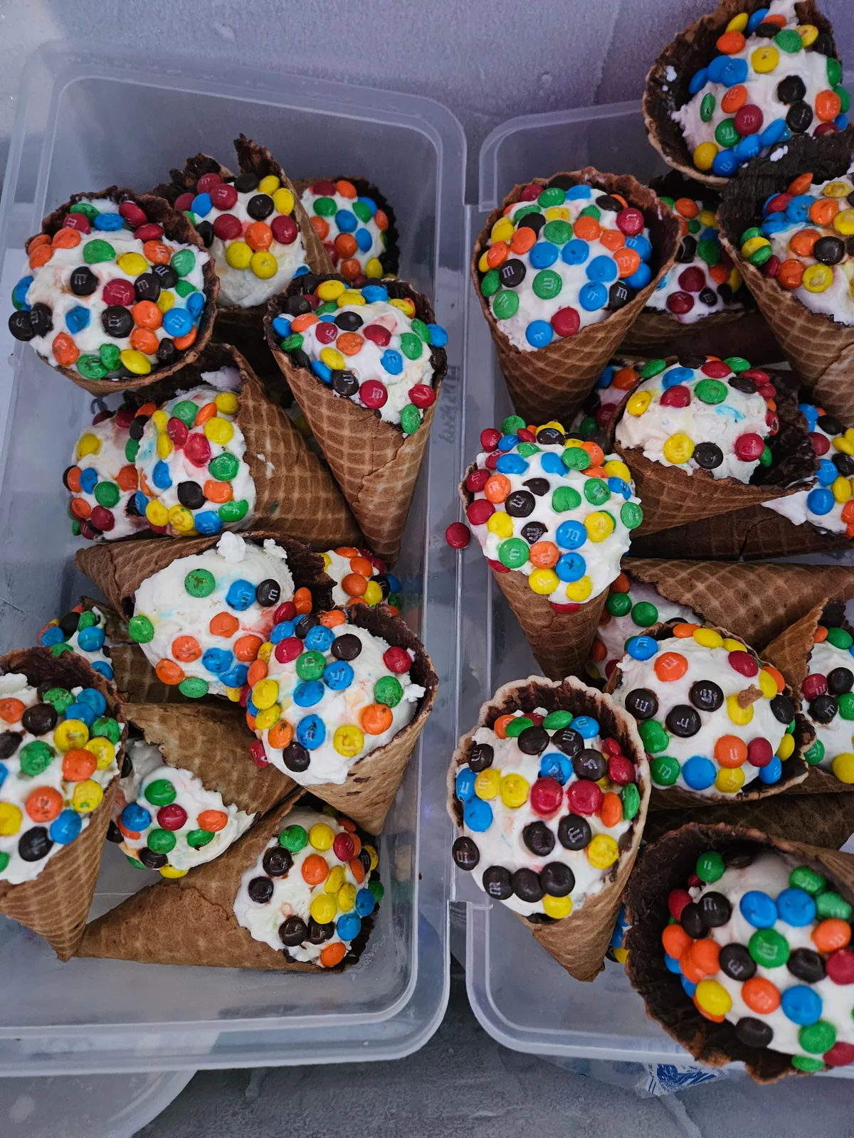 Trays of waffle cones rim-dipped in white chocolate and M&Ms, ready for scoops