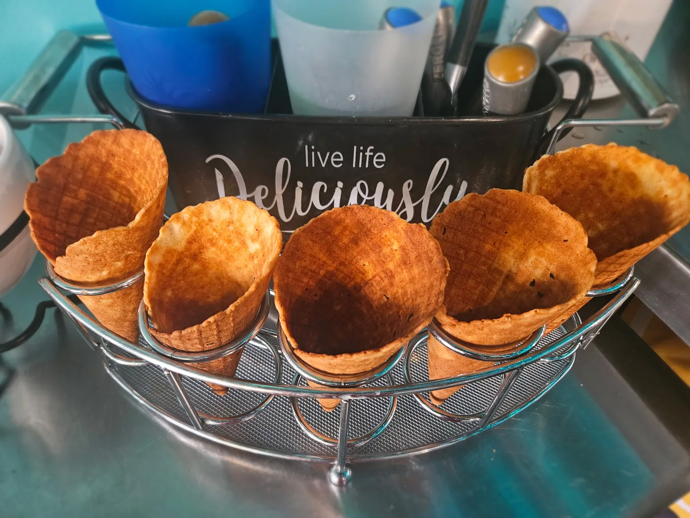 Basket of fresh-pressed waffle cones beside a Live Life Deliciously tin